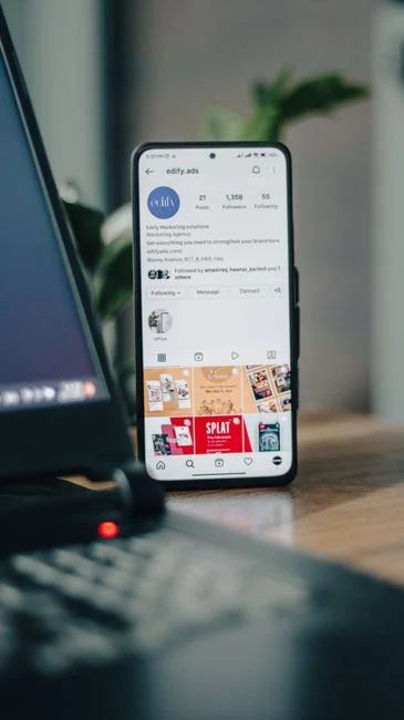 Hands using smartphone beside laptop with stock charts, showcasing digital trading.